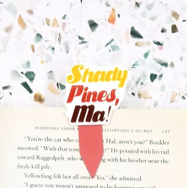 a magnetic bookmark clipped to the page of a book. yellow, red, and brown text on the bookmark says "Shady pines, Ma!"