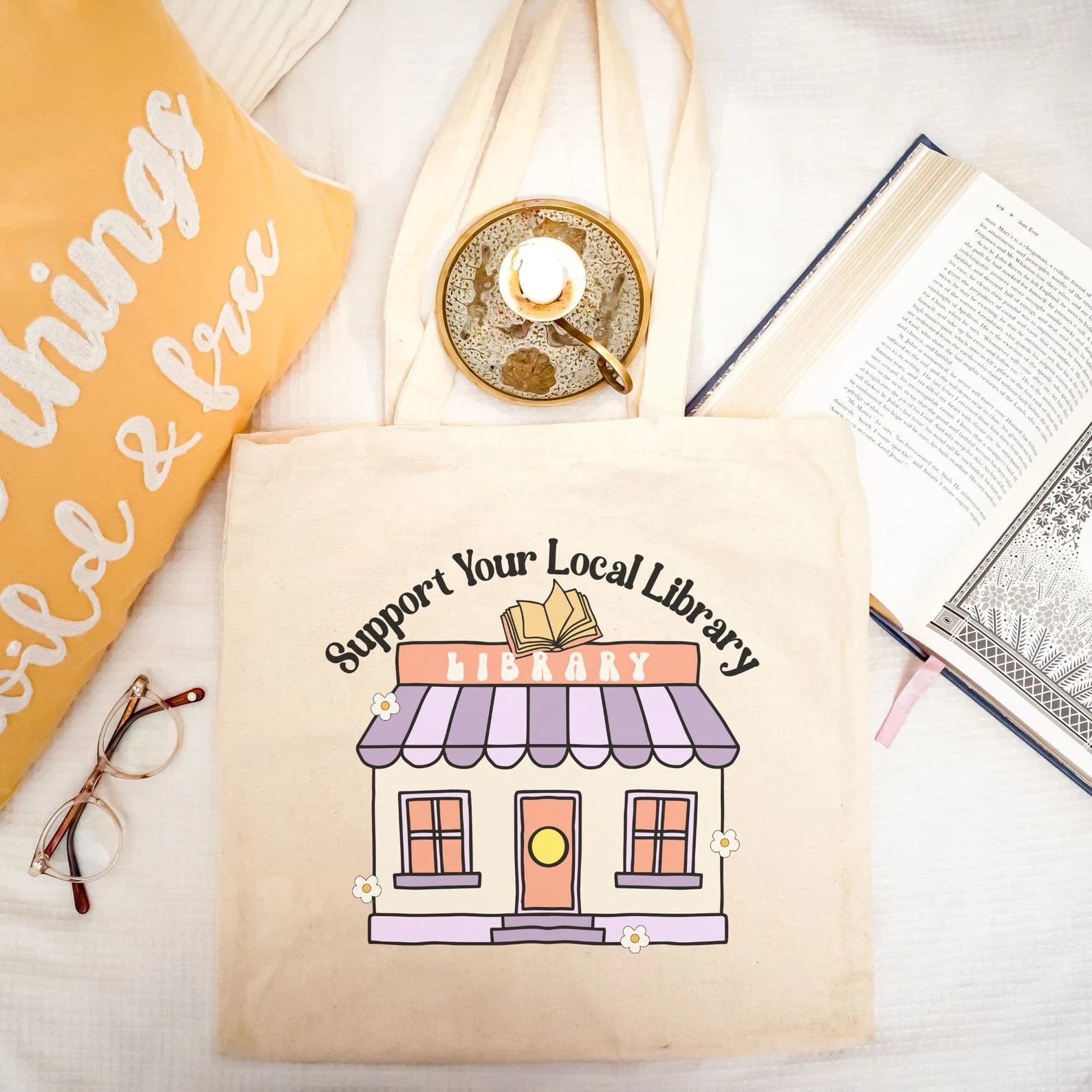 support your local library tote bag. It features a cute illustration of a library with the words "support your local library."