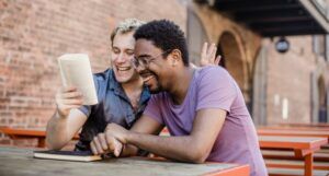 two men laughing while reading a book outdoors