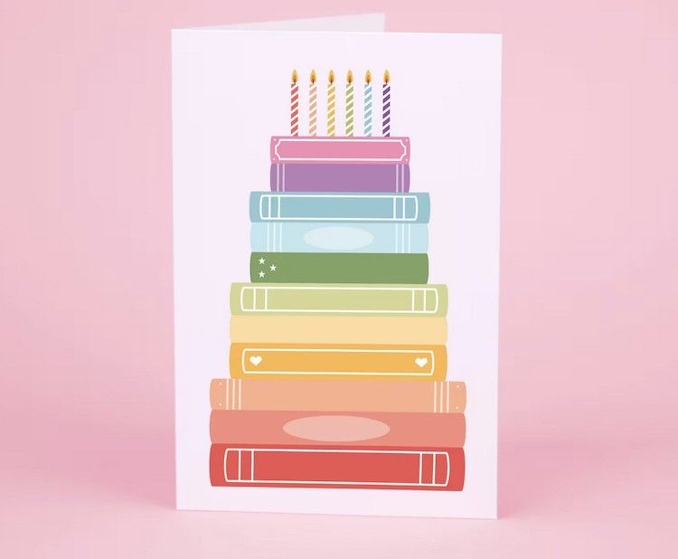 illustrated greeting card of books stacked like a birthday cake with candles on top, each book is a different color