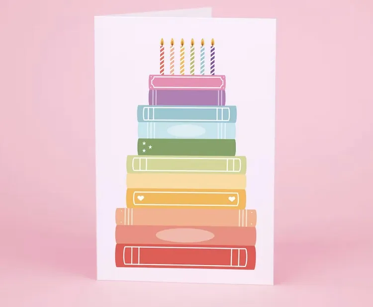 illustrated greeting card of books stacked like a birthday cake with candles on top, each book is a different color