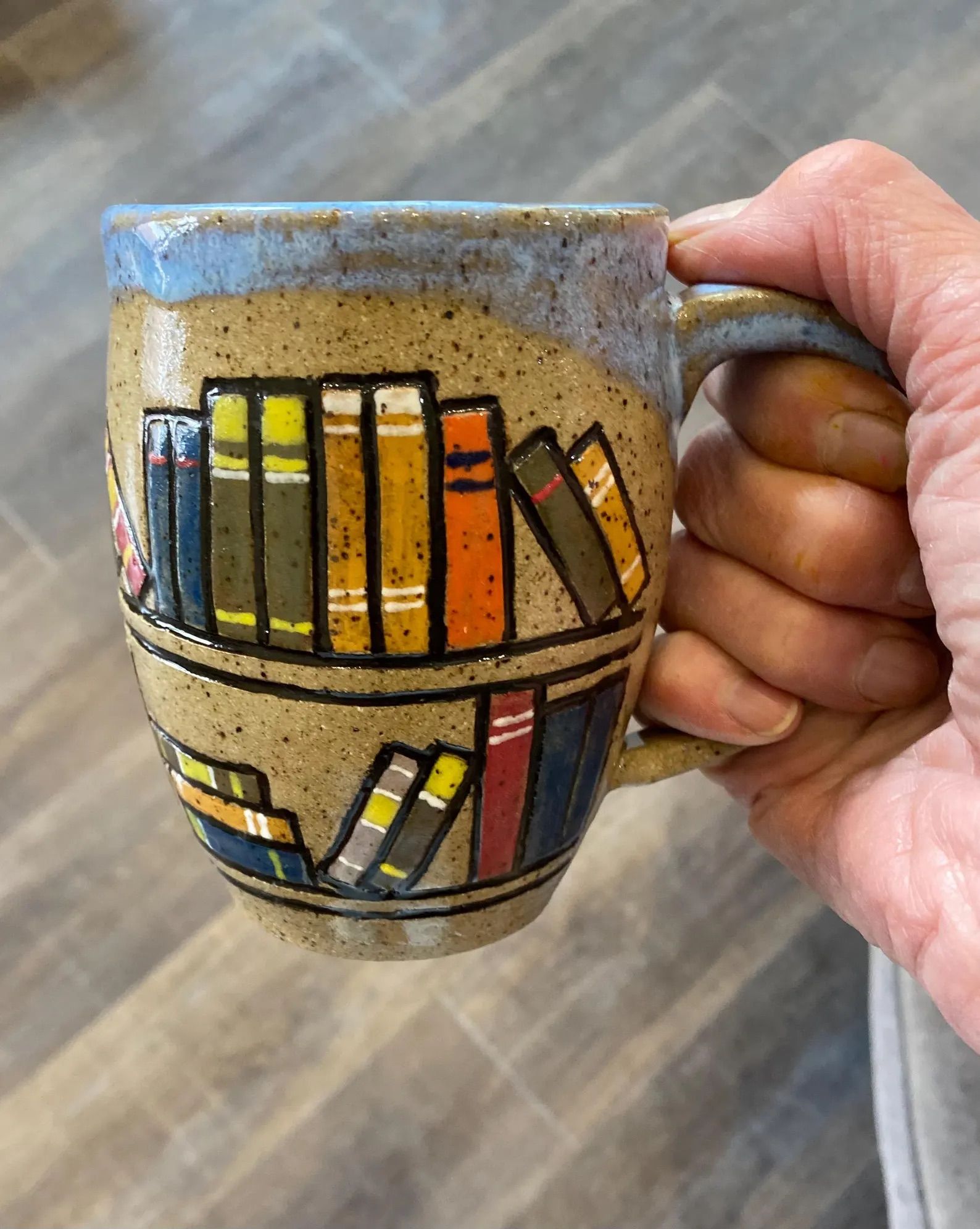 Hand Made Ceramic Book Mug in a hand in front of a wood floor.