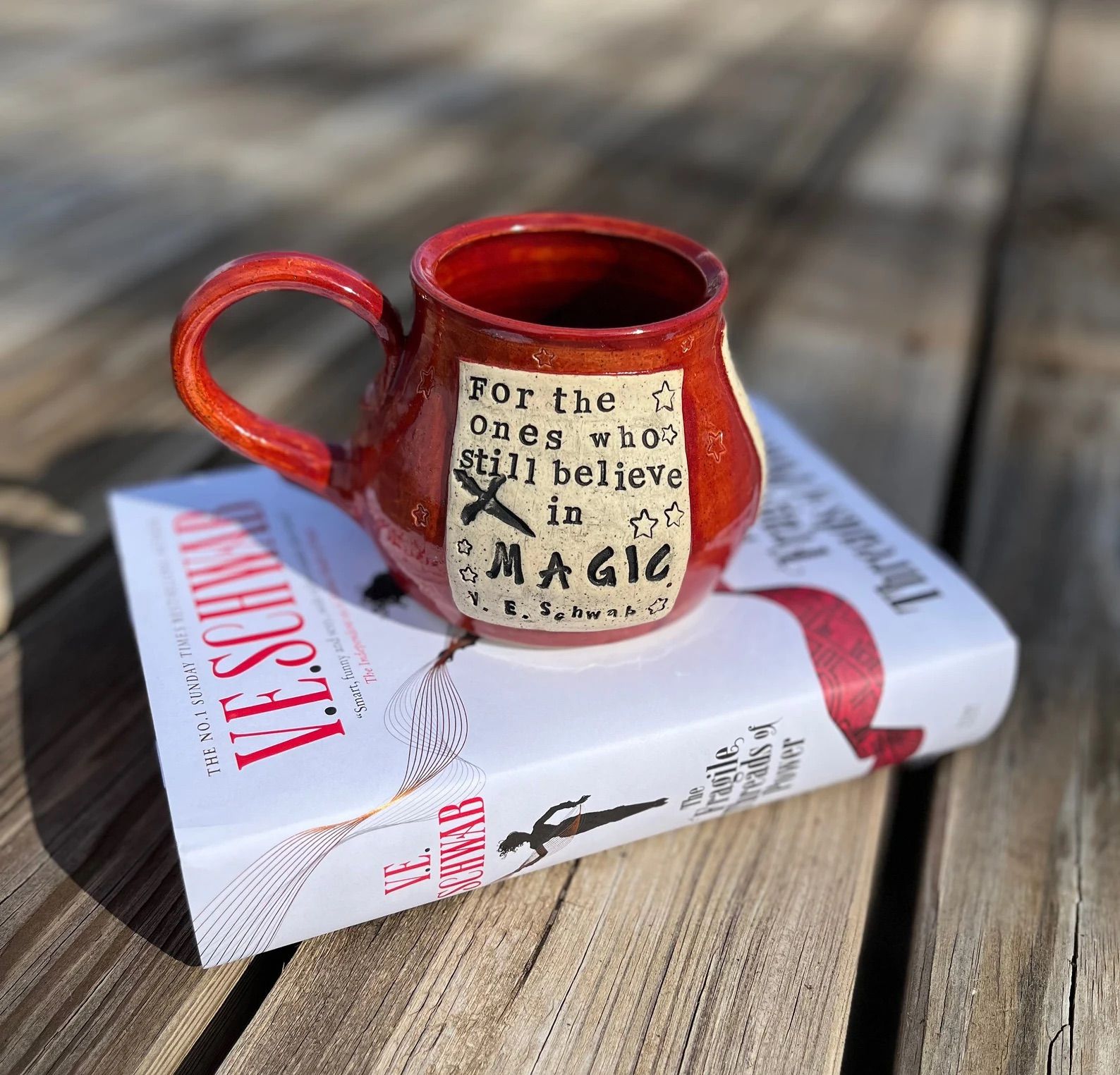 Literary Mug, The Fragile Threads of Power, Still Believe in Magic, V. E. Schwab on top of the book.