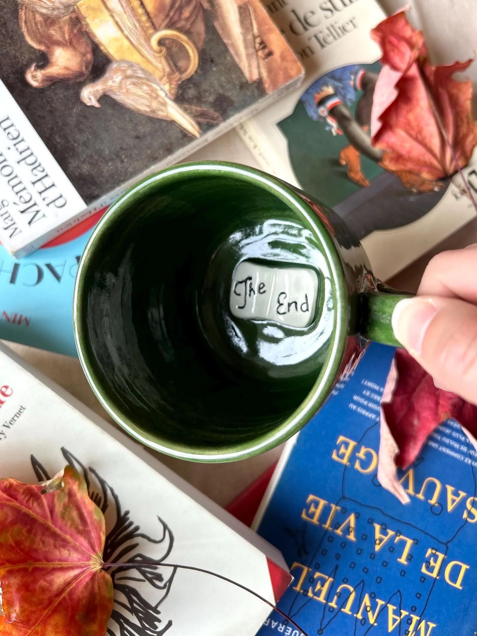 Green mug with a the end book at the bottom on top of a pile of books.