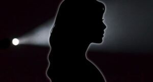 black silhouette of woman against a black backdrop with flashlight shining