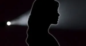black silhouette of woman against a black backdrop with flashlight shining