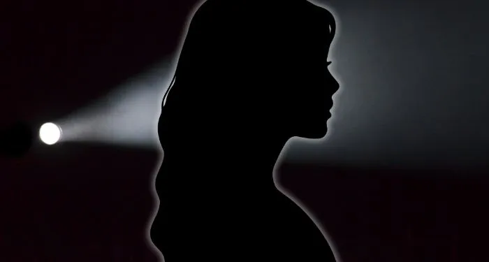 black silhouette of woman against a black backdrop with flashlight shining