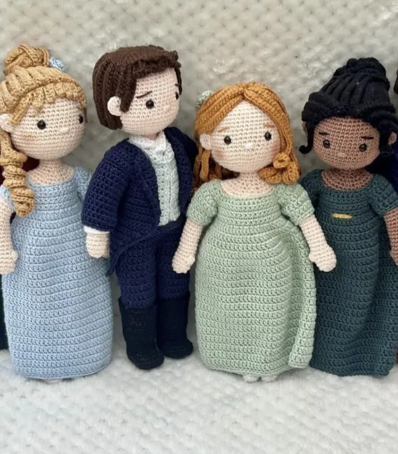 Crocheted figurines of the characters from the Bridgerton series including Daphne, a blonde white woman in a blue dress, Colin, a brunette white man in a navy suit, Penelope a red head in a green dress, and Kate, an Indian woman with black hair in a dark teal dress. 