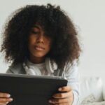 brown-skinned Black woman with fro looking at a tablet