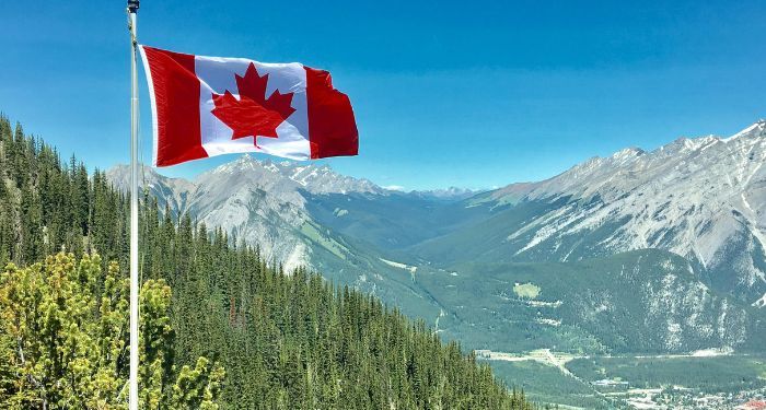 canadian flag flying against backdrop of forested mountains