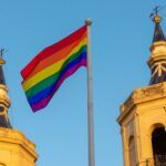 Image of two church towers with a rainbow flag flying between them