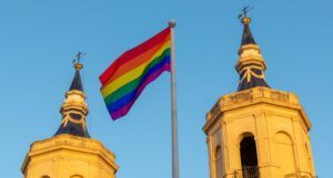 Image of two church towers with a rainbow flag flying between them