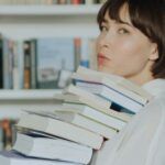 fair skinned Asian woman with a bob holding a stack of books