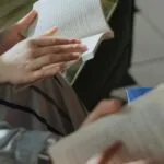 hands of two people reading books with more books on table