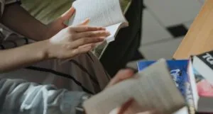 hands of two people reading books with more books on table