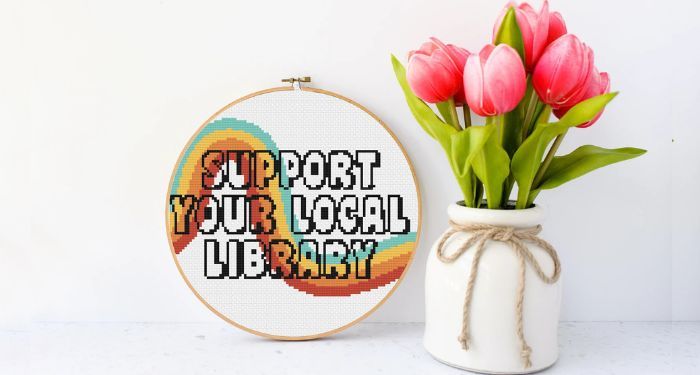 image of a colorful cross stithc that says "support your local library" beside a vase of tulips