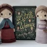 Four little crocheted aigurumi figures wearing historical dresses in the style of the American Civil War and designed to look like Amy, Meg, Beth, and Jo from Little Women. The figures are set around a beautiful green edition of the book, The Little Women.