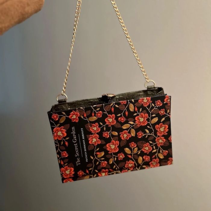 a bag made out of a black, red, and gold cover of The Secret Garden with a gold crossbody chain strap