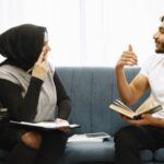 two Middle Eastern people with light tan skin (a man and a woman) sitting and discussing a book