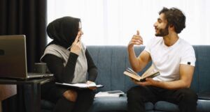 two Middle Eastern people with light tan skin (a man and a woman) sitting and discussing a book