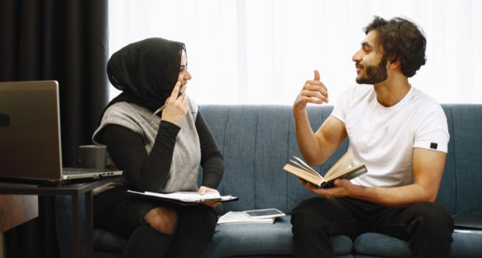 two Middle Eastern people with light tan skin (a man and a woman) sitting and discussing a book