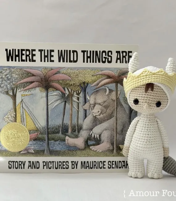 A little crocheted figurine of Max stands next to a book of Where the While Things Are. He's wearing his monster suit and a yellow crown.