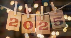2025 on pieces of brown paper clipped to laundry line with dots of light against semi-transparent book stack