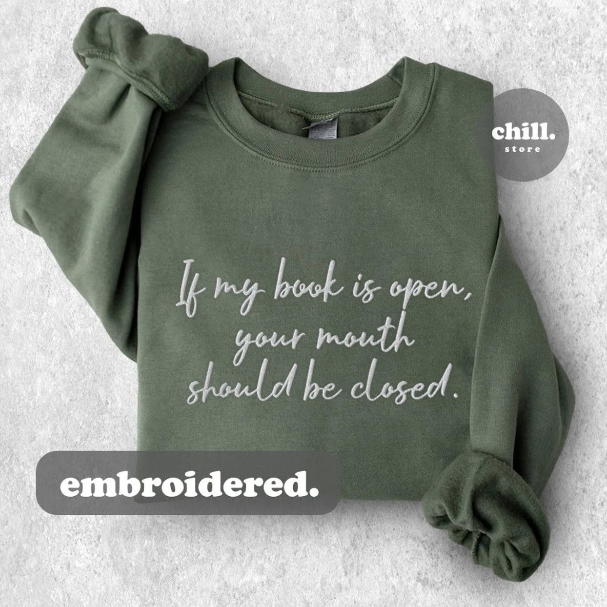 Image of a sage green crewneck sweatshirt with white cursive font that says "If my book is open, your mouth should be closed."