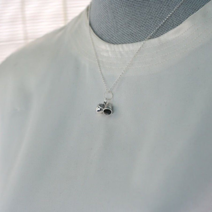 A necklace with acorn and thimble charms on a mannequin form