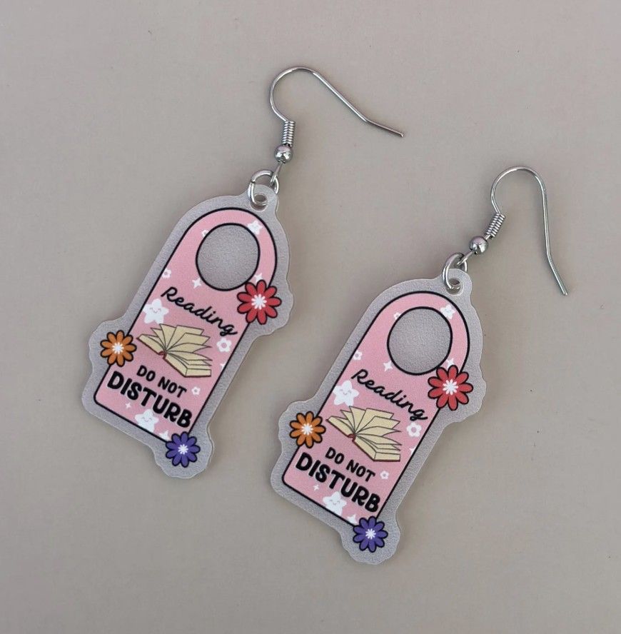 Image of a pair of dangly earrings that look like hotel door hangers that say "Reading, do not disturb"