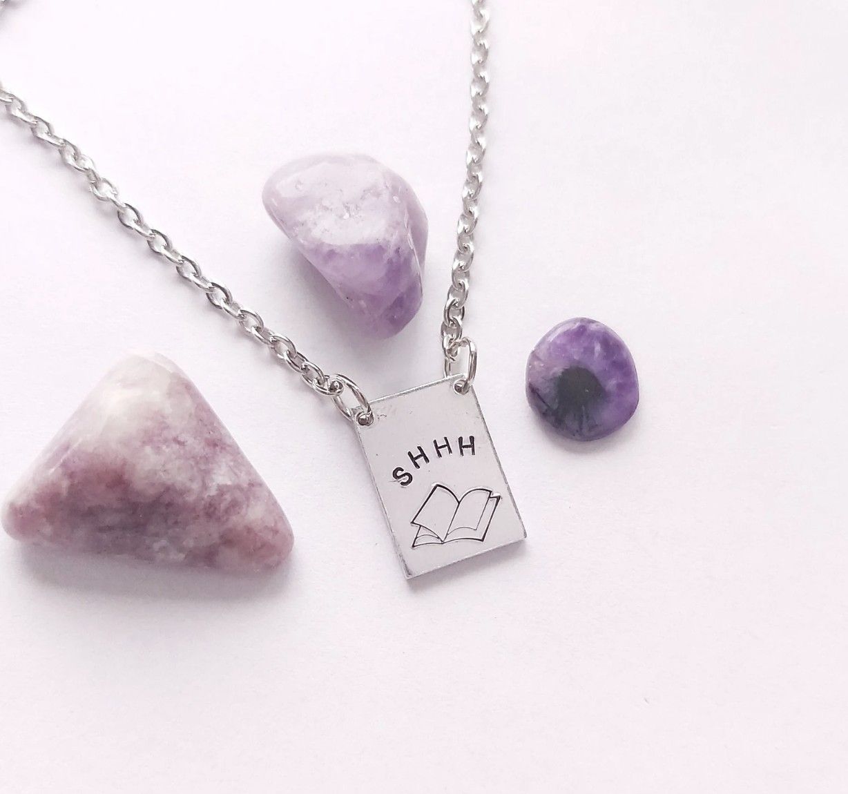 Image of a silver necklace with a charm imprinted with a book and shhh