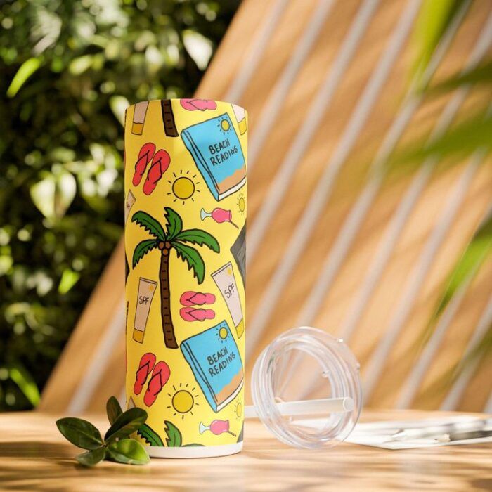 image of a green, outdoor speace with a yellow travel cup decorated with cartoon books, flip flops, suns, and palm trees