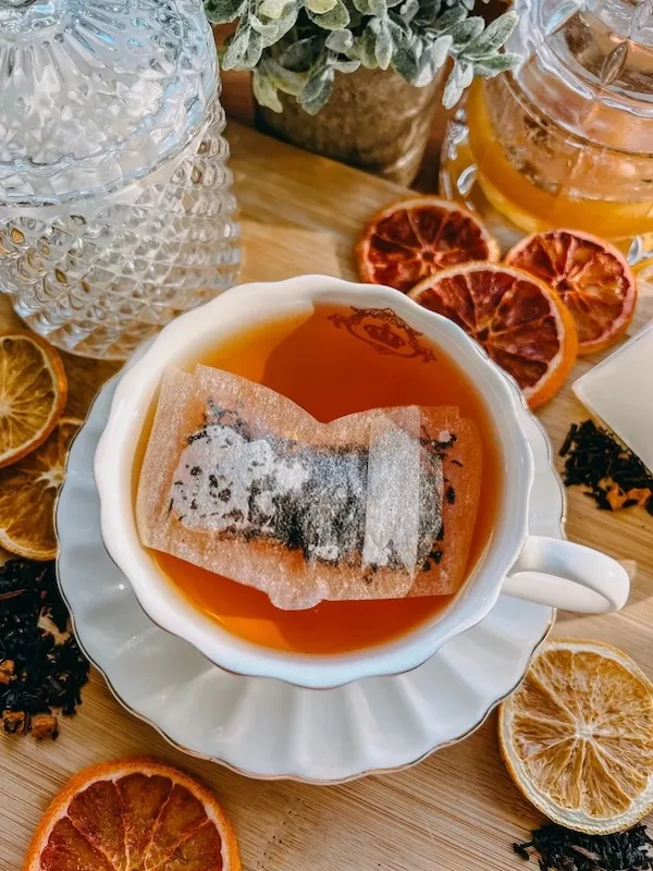 white tea cup in a saucer filled with tea with a tea bag in the shape of an open book floating on top