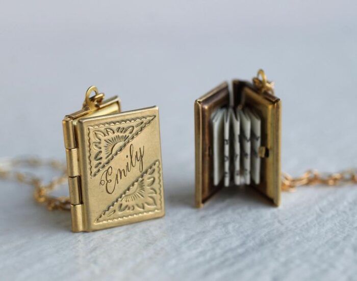image of two gold, book-shaped lockets, one showing the front cover engraved with a name, and the other showing the open locket with a tiny paper message accordion folded inside