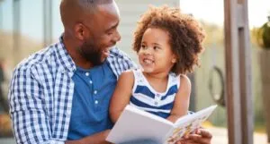 a brown-skinned father and child reading a book together and laughing