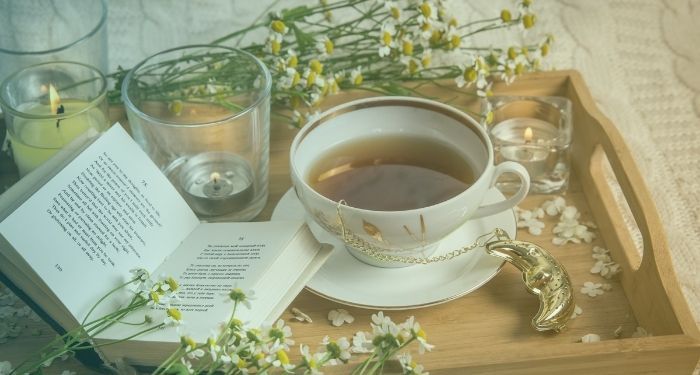 cup of tea with chamomile stems candles and book of poetry on tray with green and yellow gradient