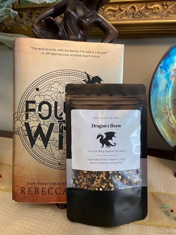 a black resealable pouch of loose leaf tea with a label for Dragon's Brew tea. Behind the bag is a hardcover copy of Fourth Wing by Rebecca Yarros