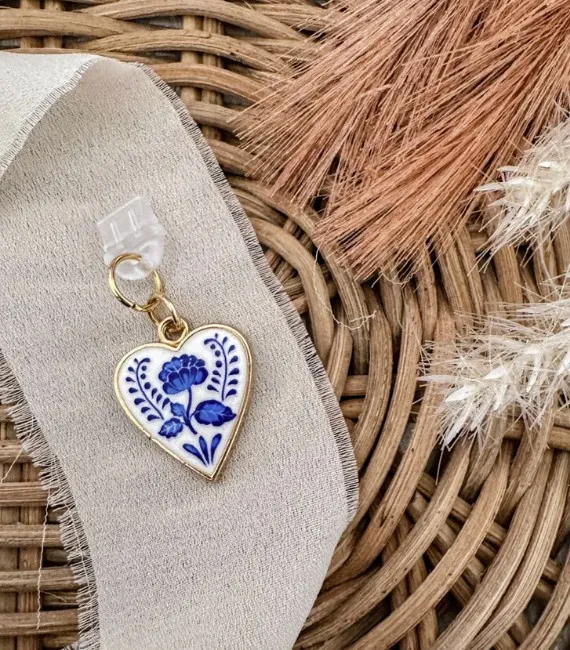 This picture features a kindle dust plug charm. It's a white heart with a blue flower in the center set against a gray ribbon.