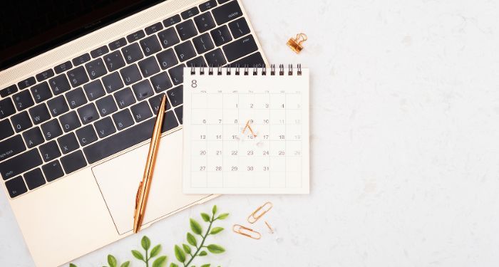 laptop with calendar on top with gold pen and paper clips on white marble counter