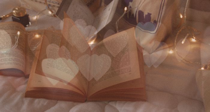 overlay of glowing hearts on image of books opened on bed and string lights