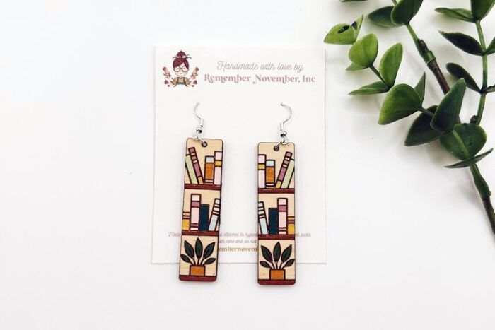 a pair of earrings- two long wooden rectangles painted to look like bookshelves with books and plants 