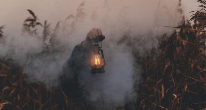 pale-skinned person holding. kerosene lantern in a smoky wheat field