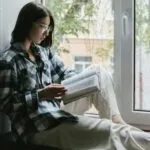 fair-skinned woman reading the bible in the windowsill