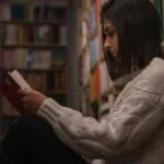 pale-skinned woman with a bob sitting in library reading between the stacks