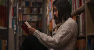 pale-skinned woman with a bob sitting in library reading between the stacks
