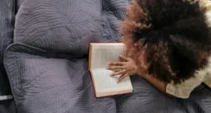 a tan-skinned person with a big afro lying on their tummy and reading a book