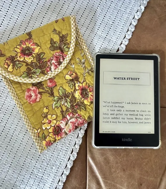 A kindle sits on a table next to a gorgeous quilted yellow floral Kindle cover