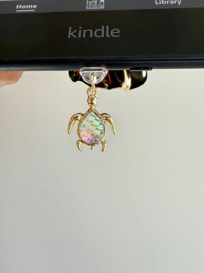 image of a kindle with a crystal, iridescent and gold sea turtle charm hanging from the USB connection