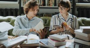 two people talking over a pile of books
