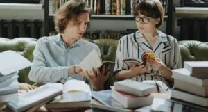 two people talking over a pile of books